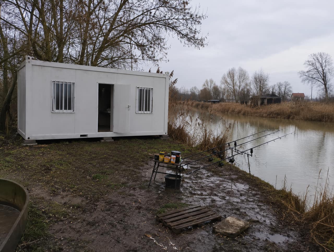 Konténer horgászház sáros, esős tóparton, ahol a bejárat mögé be lehet húzódni